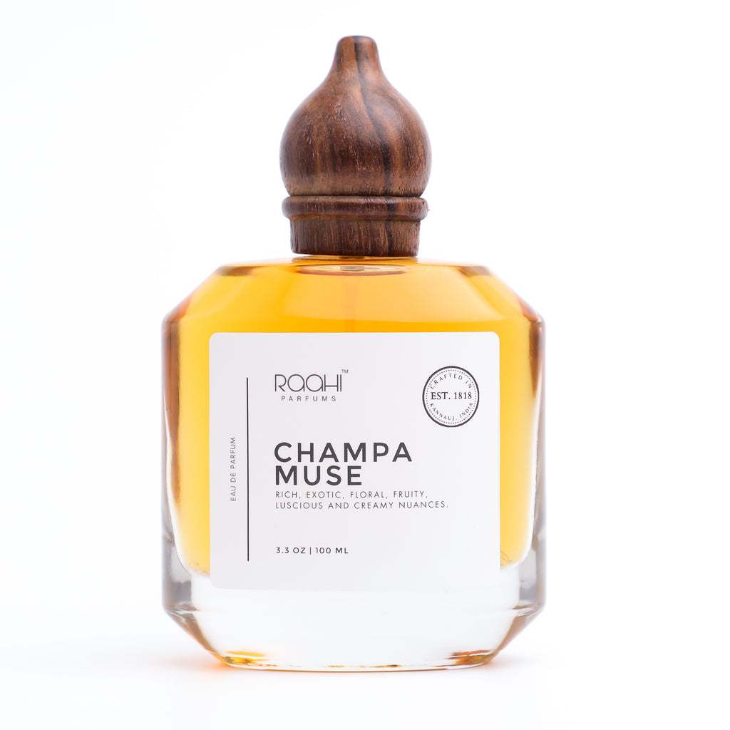 A clear glass bottle with a dark wood cap containing amber perfume labeled champa muse by raohi parfums eau de parfum
