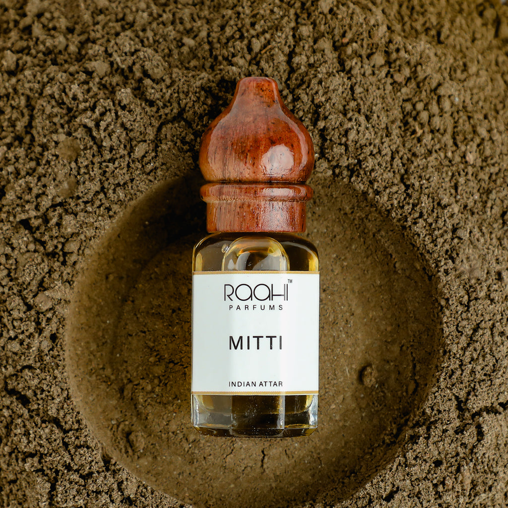A clear glass bottle of amber mitti attar with a polished wooden stopper handcrafted in kannauj by roahi parfums