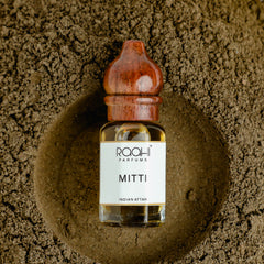 A clear glass bottle of amber mitti attar with a polished wooden stopper handcrafted in kannauj by roahi parfums