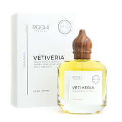 A clear glass bottle of vetiveria eau de parfum with golden-yellow liquid and dark brown wooden stopper beside white packaging