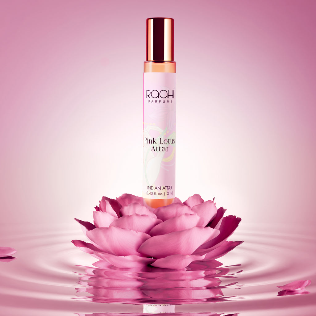 A slender transparent glass bottle with rose gold cap and label containing amber pink lotus attar by raah parfums 12ml