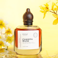 A sleek transparent glass perfume bottle with dark wooden stopper and white label champa muse by roohi parfums