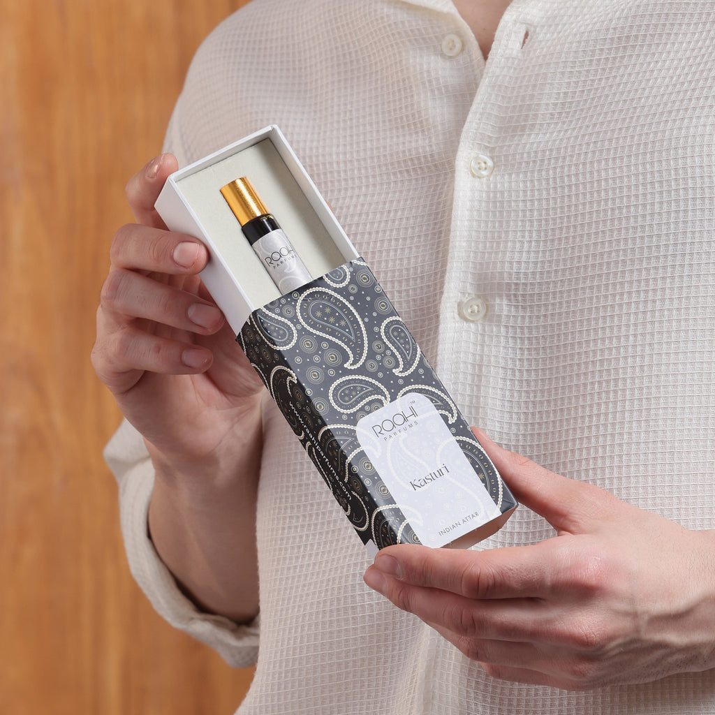 A sleek black and white paisley box holding a roqi kasturi perfume rollerball with a gold cap handcrafted in Kannauj