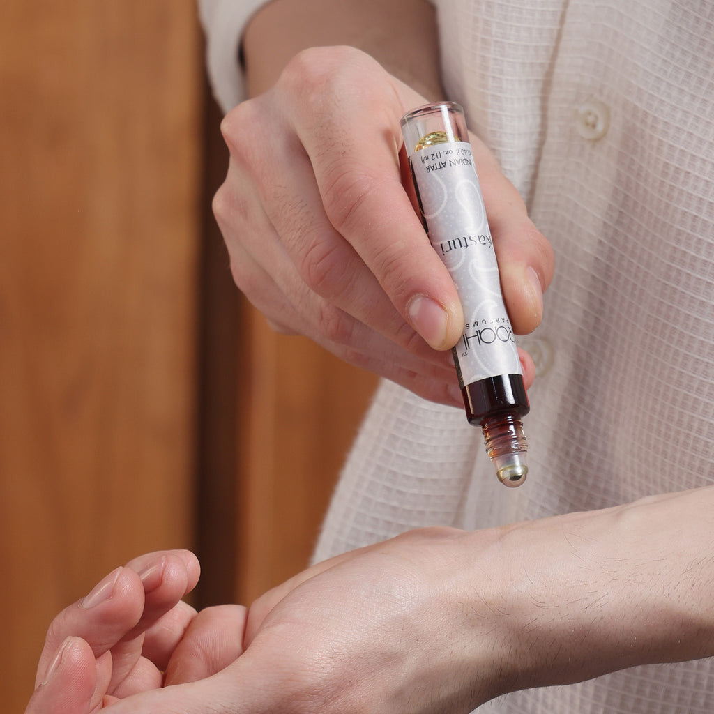 A sleek transparent glass rollerball bottle with silver cap and black base containing dark kasturi attar liquid