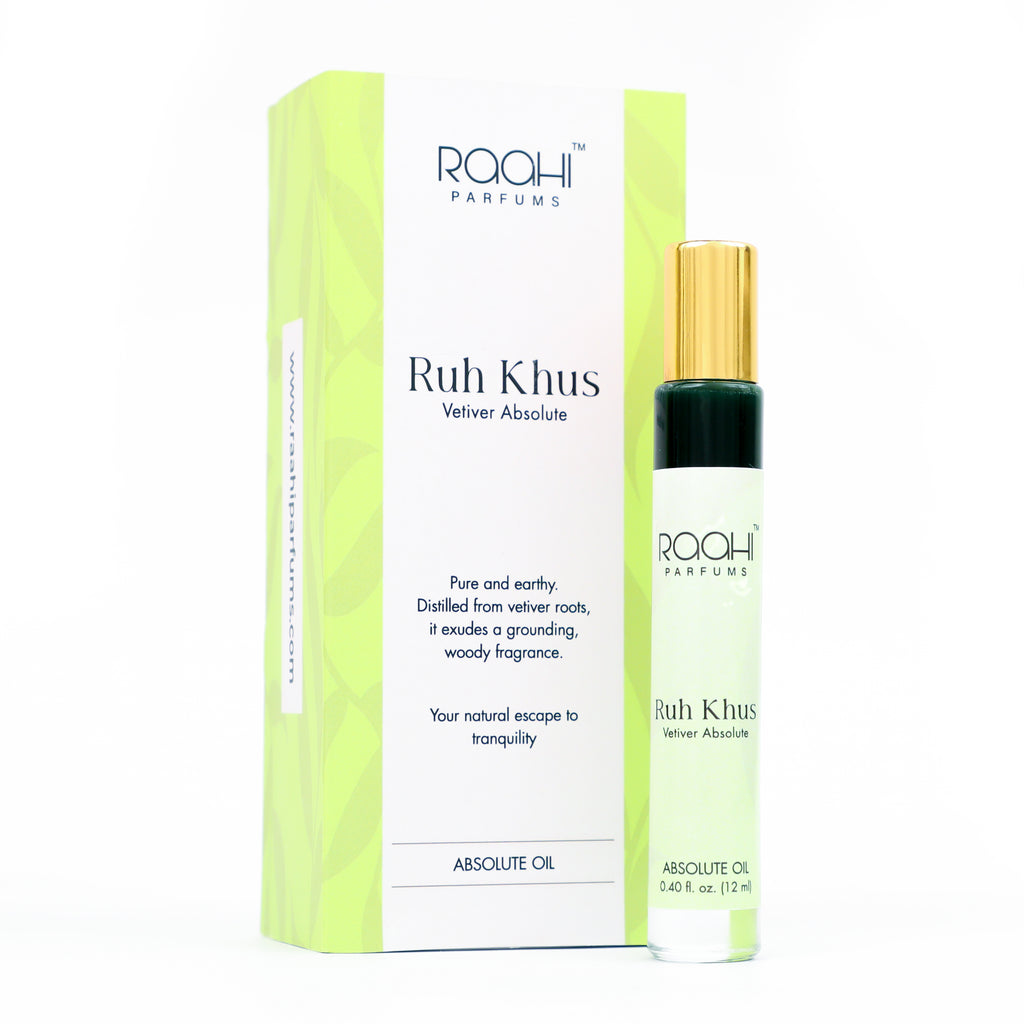 A sleek transparent glass rollerball bottle with gold cap and green band containing mint-green vetiver absolute oil