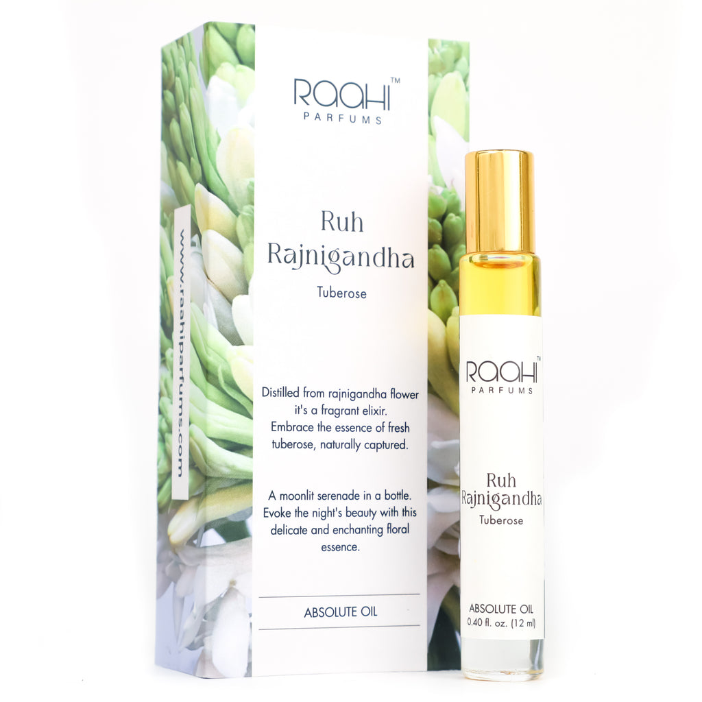 A sleek transparent glass rollerball bottle with golden cap and white label containing ruh rajnigandha tuberose absolute oil