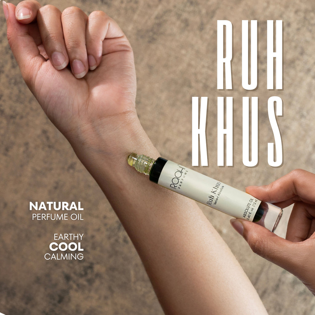 A sleek white cylindrical rollerball bottle with black cap and gold roll-on applicator labeled ruh khus by rooth parfums