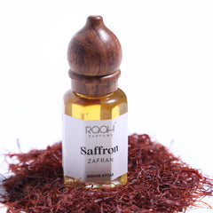 A small glass bottle with a dark brown wooden stopper labeled saffron zafaran indian attar by raahi parfums handcrafted in kannauj