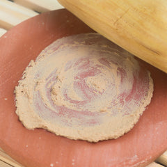 A circular beige sandalwood clay dough with red swirls resting on a terracotta plate for rubbing use