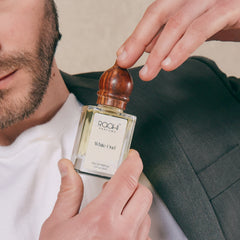 A clear glass bottle of raahi parfums white oud eau de parfum 50ml with polished wooden cap and minimalist white label
